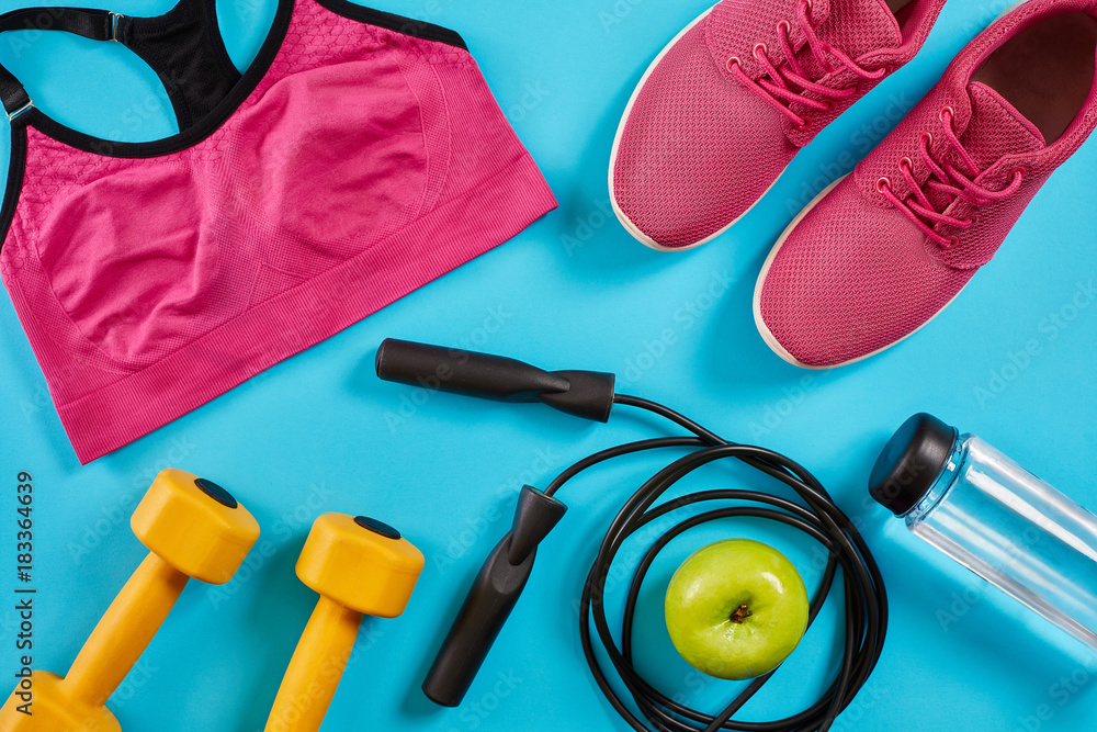 Athlete's set with female clothing, dumbbells and bottle of water on bright blue background