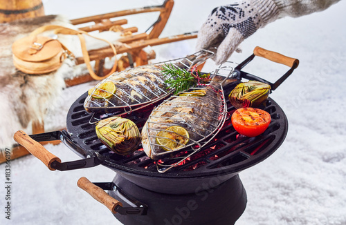 Two whole fish grilling over a winter barbecue