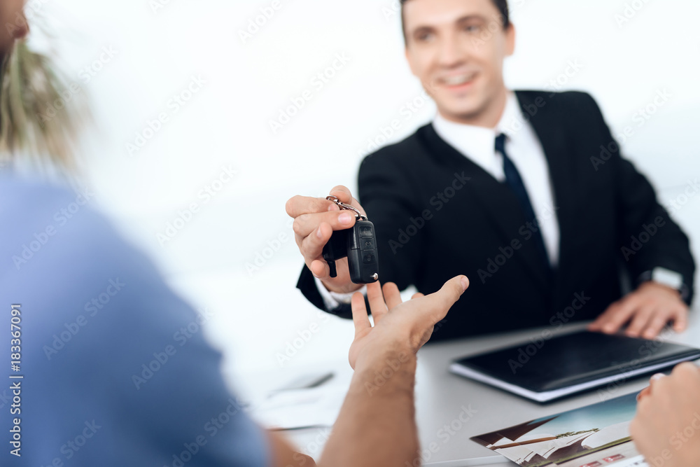 The seller in the car showroom gives the car keys to the buyer. The seller in the car showroom gives the car keys to the buyer.