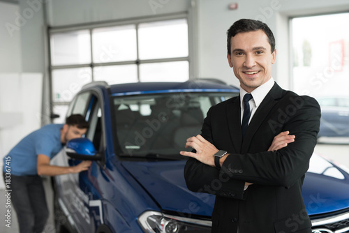 A car salesman is posing for a camera near buyers who are choosing a new car. © VadimGuzhva
