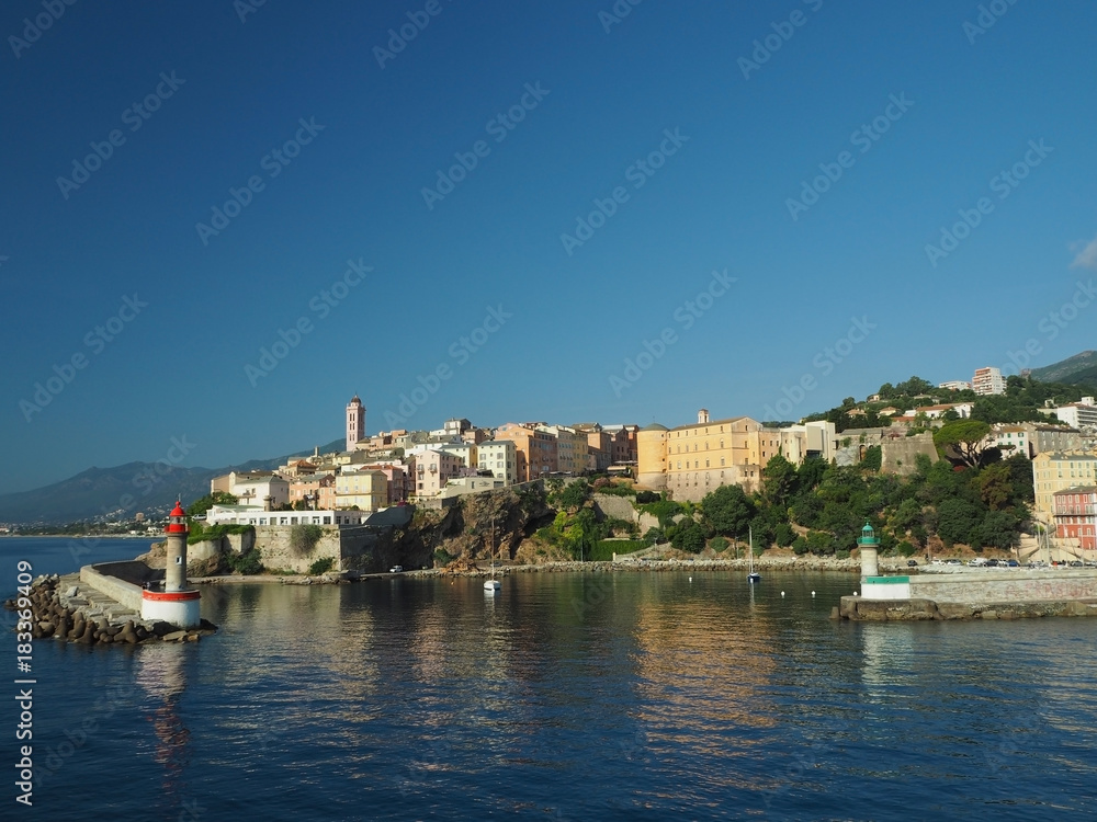 Corsica Bastia port view from sea on harbour with red and green lighthous church and old town blue sky background