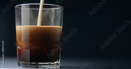 Mixing coffee, hot chocolate and steamed milk into a large glass to make a hot drink on light gray background