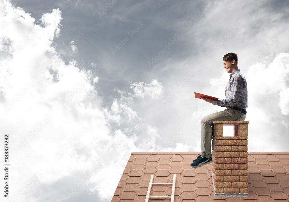 Handsome man on brick roof against cloud scape reading book Handsome man on brick roof against cloud scape reading book