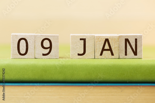 Wooden cube shape calendar for JAN 9 on green book, table. 