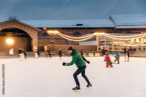 Cheerful bearded man spends Christmas time on majestic ice rink decorated with lights, skates on ice, has fun, enjoys his hobby and snowy winter weather. People, leisure, active lifestyle concept © VK Studio