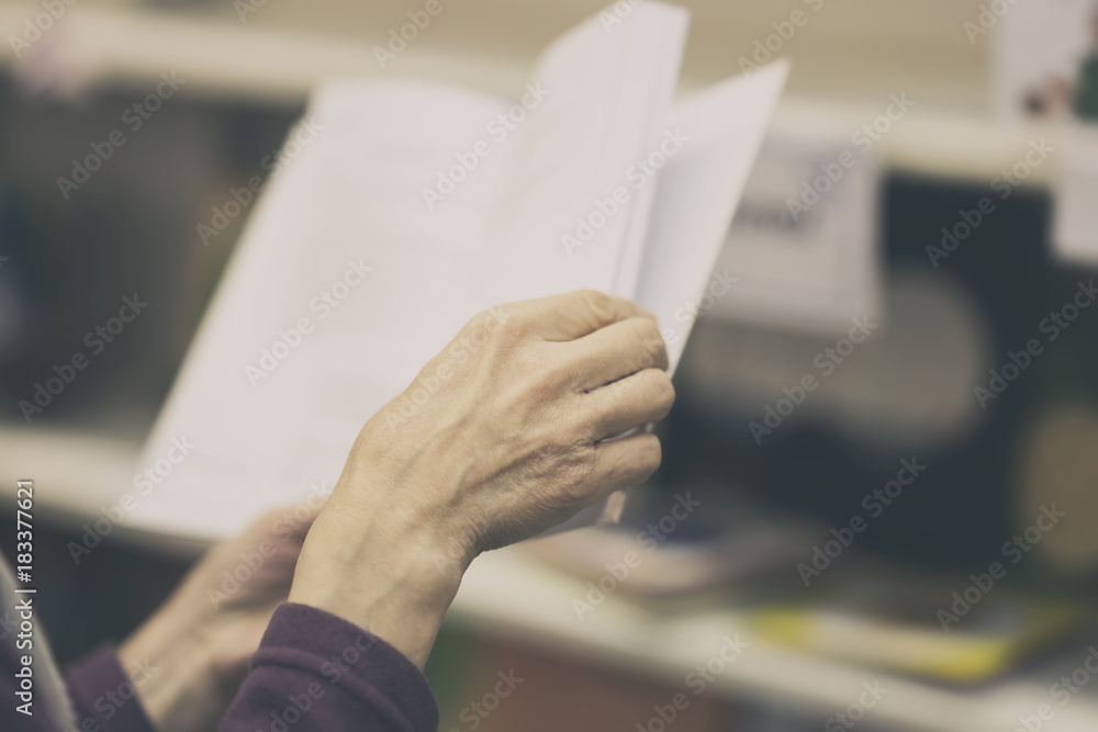 Close-up of hands of elderly person with open book, library. Toned background. Education concept, Self-study, reading fiction, pension, interests in elderly, life style