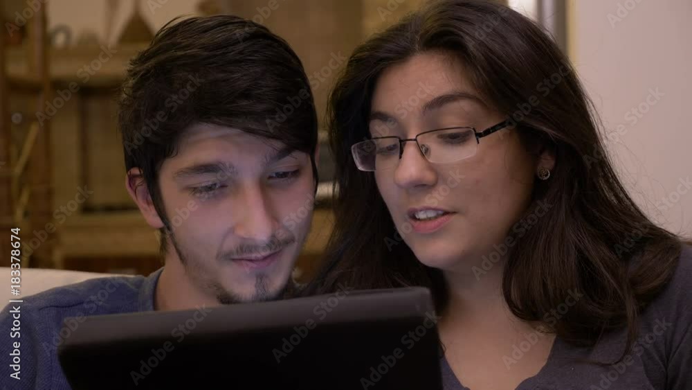 Romantic adult couple using tablet pc at home on the couch watching online comedy movies on Saturday night Romantic adult couple using tablet pc at home on the couch watching online comedy movies on Saturday night