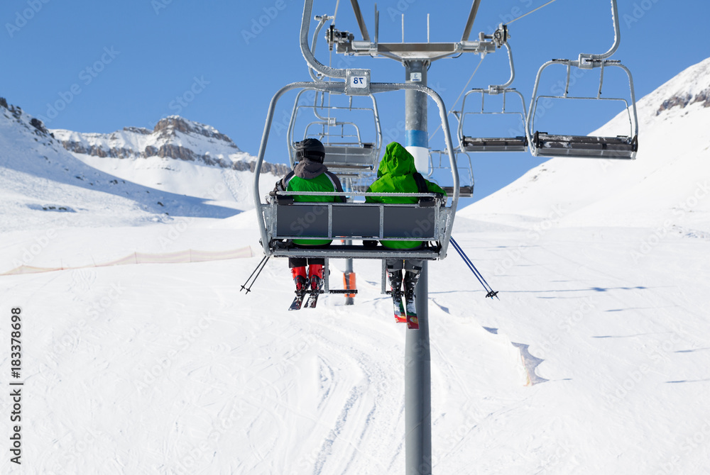 Two skiers on chair-lift and snow ski slope Two skiers on chair-lift and snow ski slope