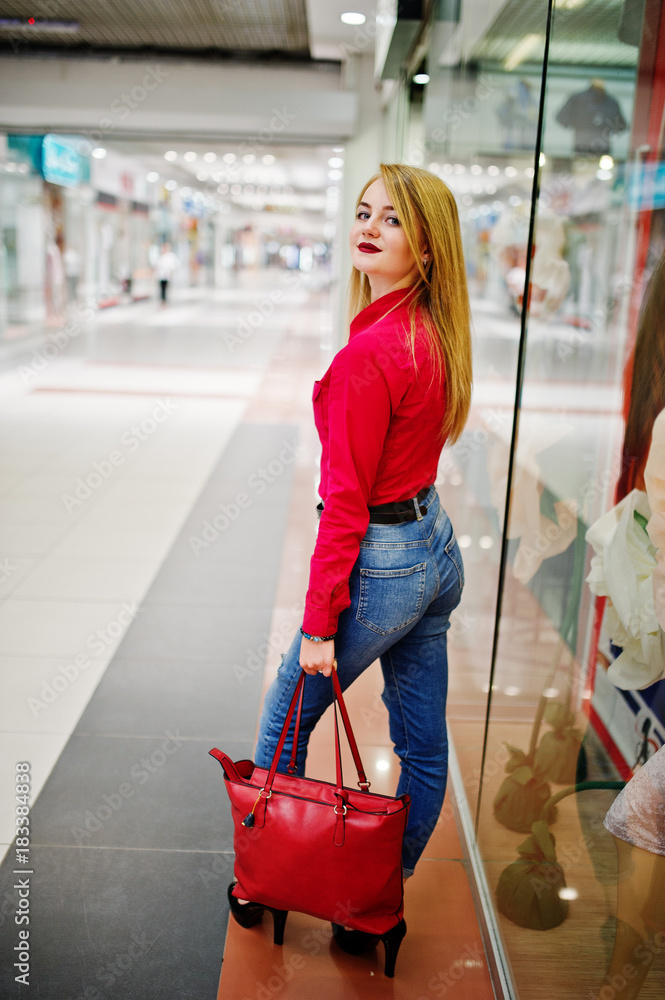 Portrait of a beautiful woman wearing red blouse, casual jeans and black  high heels poses with red leather handbag in huge shopping mall. Stock  Photo | Adobe Stock