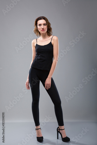 Fashion portrait of a beautiful girl in blank black T-shirt and black pants on a gray background.