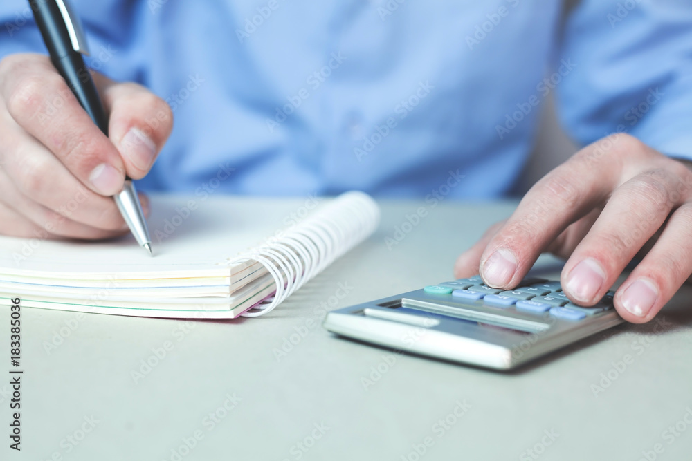 Fototapeta premium Man using calculator and writing on a notepad.