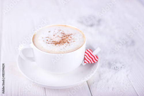 White cup of coffee cappuccino with Ceylon cinnamon and red heart on a wooden background
