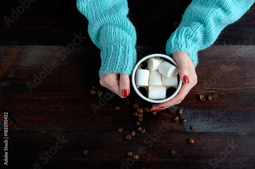 girl in blue sweater holding cup of coffee with marshmallows hands close up copy space