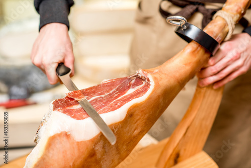 Cutting with long knife prosciutto leg in the food store photo