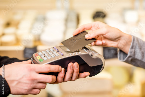 Woman paying with card contactless in the food store. Close-up view on the terminale and card photo