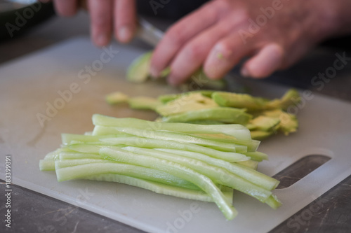 Cut cucumber and avocado on the kitchen table with a sharp knife close up. Women's hands