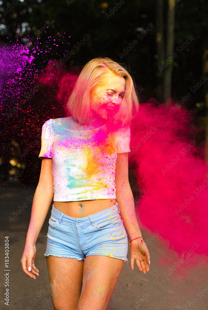 Cheerful young woman in white t shirt and jeans shorts playing with red Holi  powder exploding around her Stock Photo | Adobe Stock