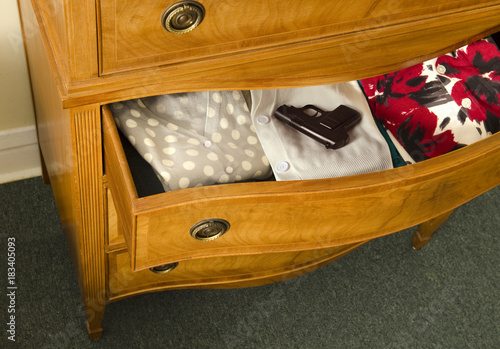 Φωτογραφία women's open dresser drawer with gun pistol on clothing