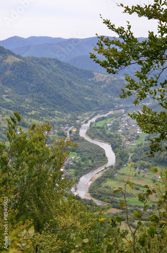 A beautiful view of the village of Mezhgorye, Carpathian region. A lot of residential buildings surrounded by high forest mountains and long river photo