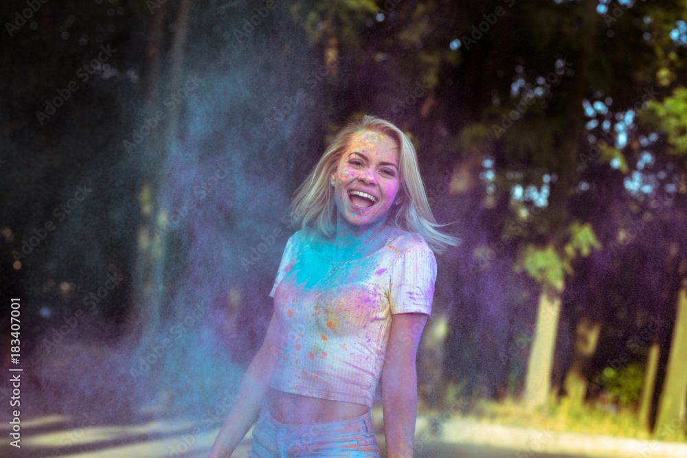 Fototapeta premium Laughing young woman with fluttering hair playing with Holi powder exploding around her