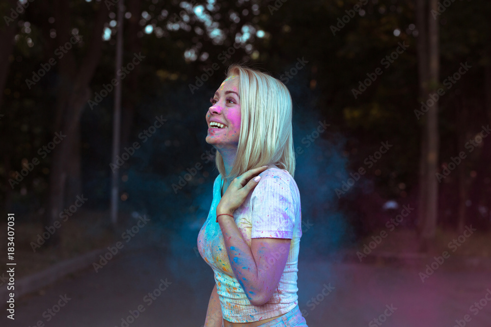 Fototapeta premium Happy blonde woman posing with Holi powder exploding around her