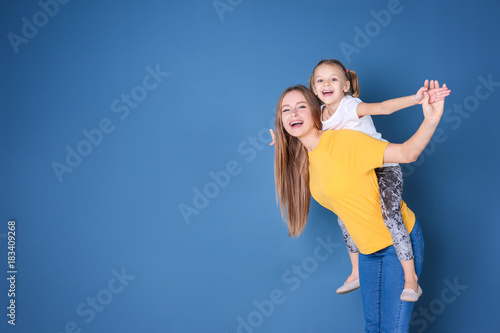 Happy mother and her daughter against color wall in children room