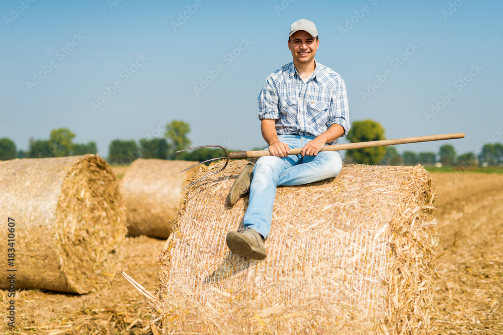 Smiling farmer sitting on hay in his field Smiling farmer sitting on hay in his field