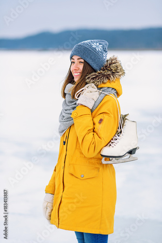 Tableau sur toile Beautiful girl in a yellow winter jacket with ice skates in the middle of a frozen lake