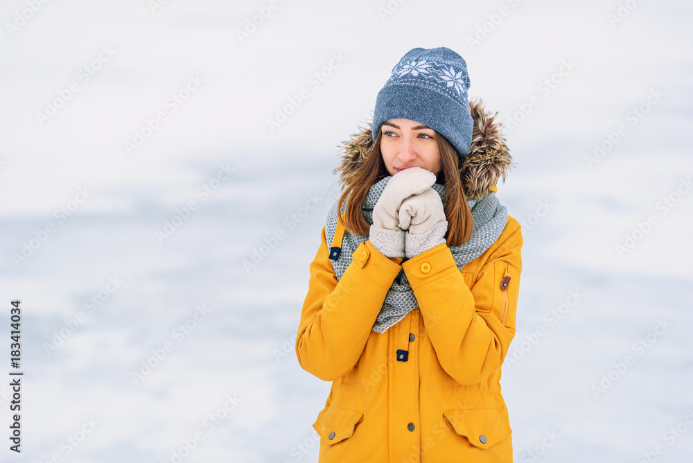 Close up portrait of beautiful smiling girl in a yellow winter jacket and warm hat on the frozen lake.