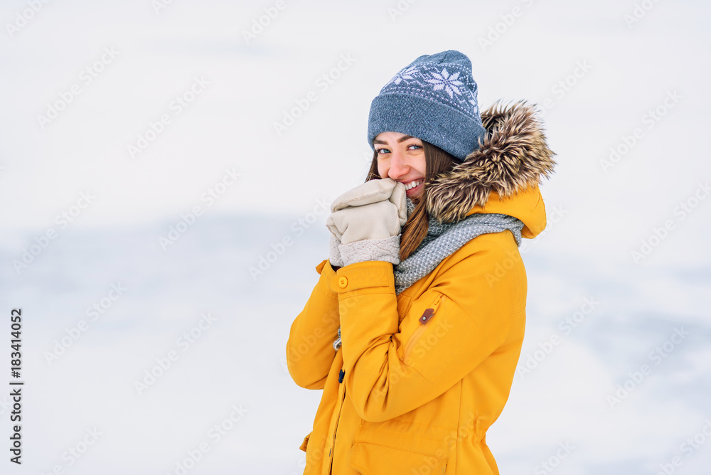 Close up portrait of beautiful smiling girl in a yellow winter jacket and warm hat on the frozen lake.