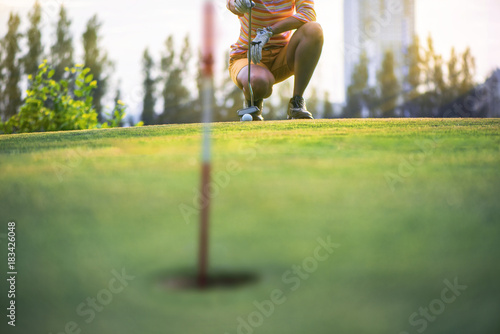 a woman golf player in calculate line measurement going to have putter on the green of golf course for a best resulted