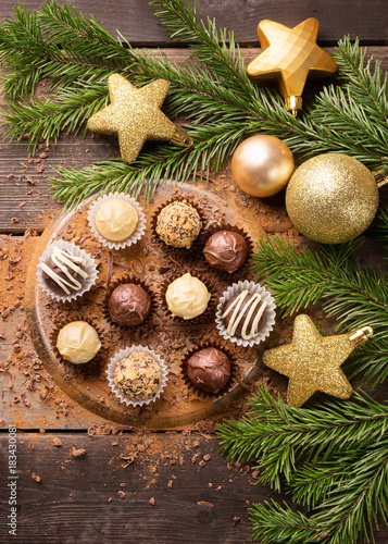 Chocolate sweets from different types of chocolate on the New Year's table. A dark wooden background is decorated with spruce branches. Christmas festive concept.