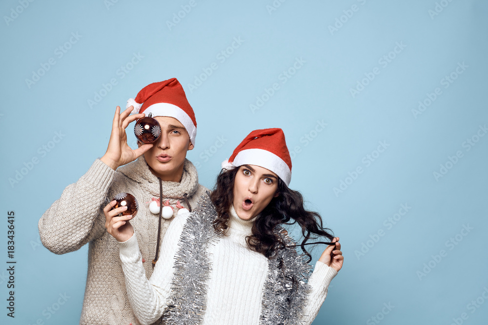 man and woman in New Year's hats holding Christmas toys, tinsel, holiday, new year, christmas, light blue background, free space for copy, couple man and woman in New Year's hats holding Christmas toys, tinsel, holiday, new year, christmas, light blue background, free space for copy, couple