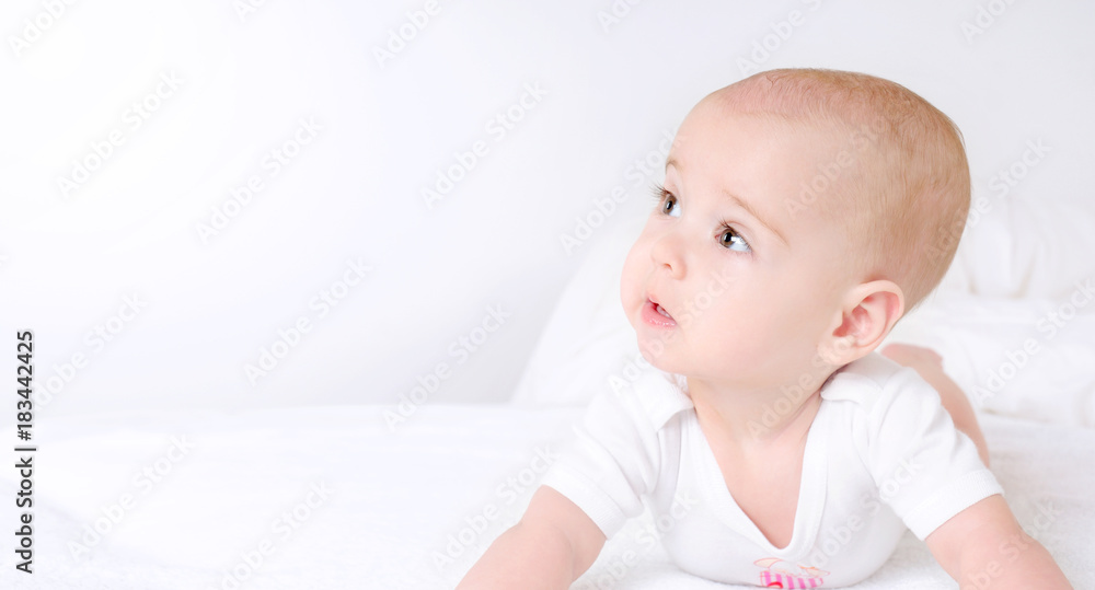 Cute baby with beautiful brown eyes lying in white bed