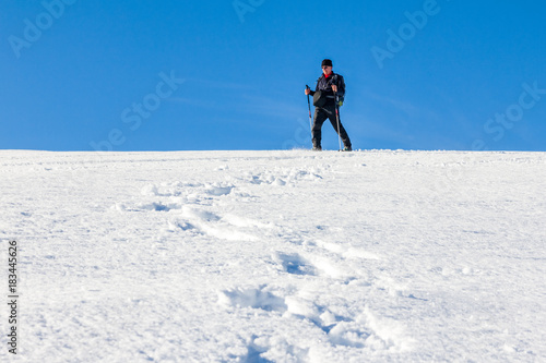 Man is snowshoe hiking through deep snow on sunny day