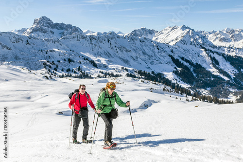Obraz na plátně Senior couple is snowshoe hiking in alpine winter mountains