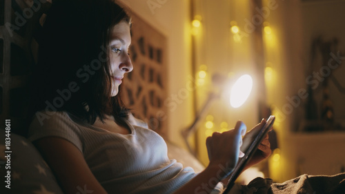 Happy smiling woman using tablet computer for sharing social media lying in bed at home at night