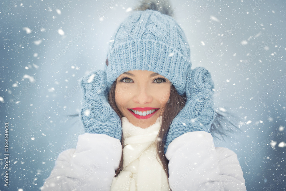 Beautiful smiling young woman in warm clothing. The concept of portrait in winter snowy weather Beautiful smiling young woman in warm clothing. The concept of portrait in winter snowy weather