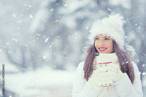 Beautiful smiling young woman in warm clothing with cup of  hot tea coffee or punch. The concept of portrait in winter snowy weather