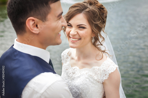 Attractive bride and groom on wedding day. Beautiful newlyweds smiling near the lake. Close-up portrait