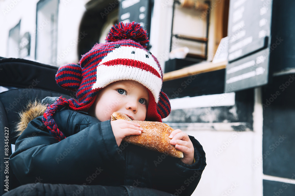 Fototapeta premium Dziecko jedzące Trdlo lub Trdelnik - tradycyjne krajowe czeskie słodkie ciasto.