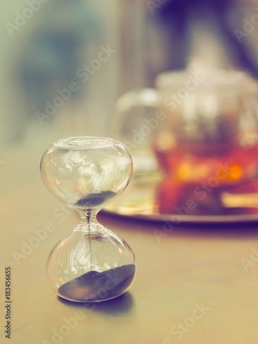 hourglass on table with de-focused tea pot ,copy space.