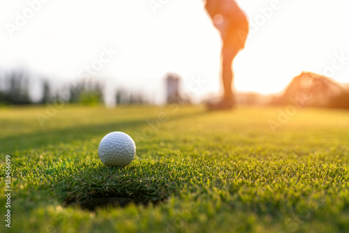 Golfer asian woman putting golf ball on the green golf on sun set evening time, select focus. Healthy and Lifestyle Concept.