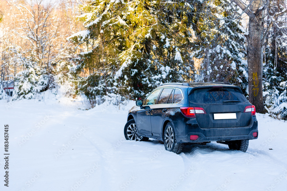Winter tires. Black Subaru Outback rear view on snowy forest road. Winter conditions.