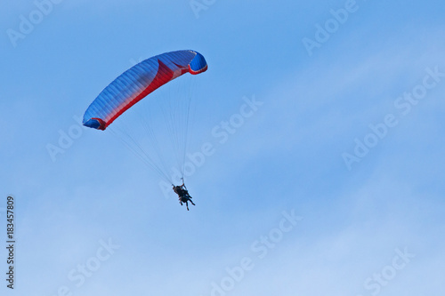 Vol en parapente avec aile bleue et rouge sur fond de ciel bleu d'été dans un brume de chaleur.