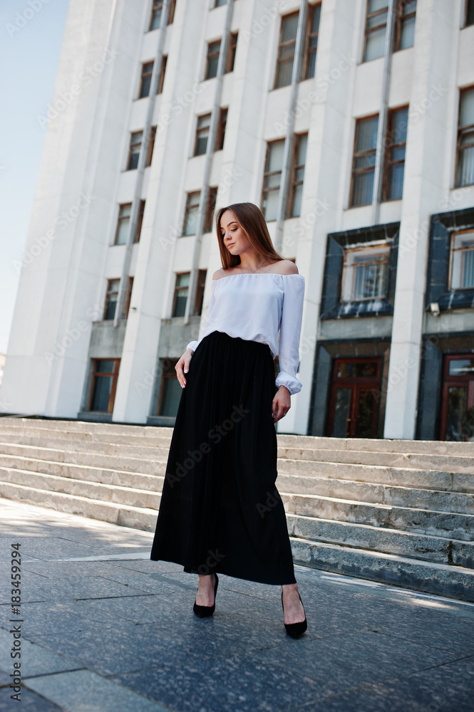 Portrait of a fabulous young successful woman in white blouse and broad black pants posing on the stairs with a huge white building on the background. Portrait of a fabulous young successful woman in white blouse and broad black pants posing on the stairs with a huge white building on the background.