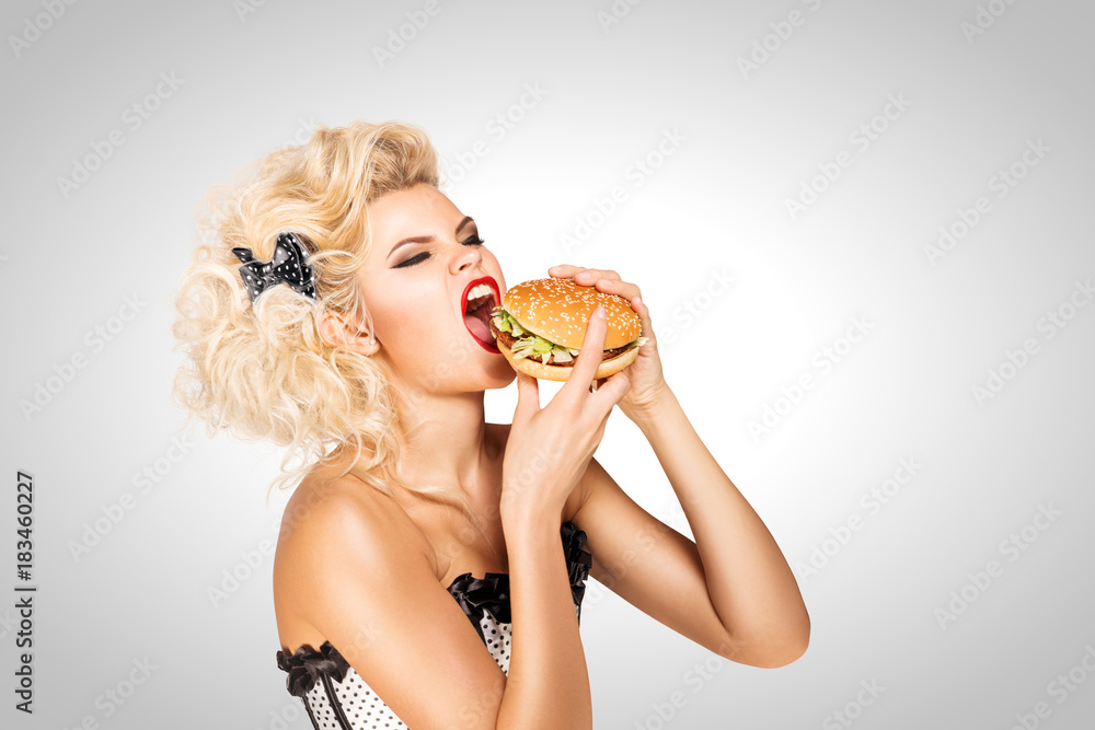 Eating burger / Beautiful pinup model eating a hamburger on grey background. Eating burger / Beautiful pinup model eating a hamburger on grey background.