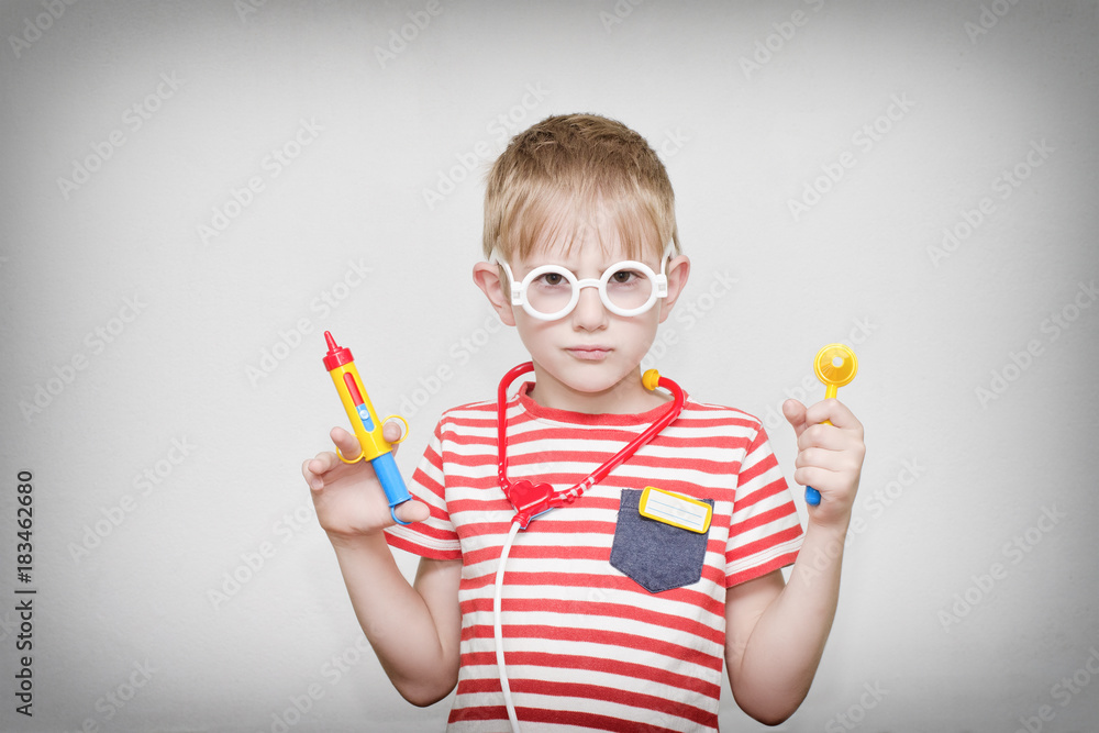 Cute boy playing doctor. Toy syringe, glasses and phonendoscope. Portrait Cute boy playing doctor. Toy syringe, glasses and phonendoscope. Portrait