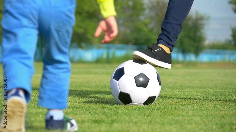 Legs of a young woman and child playing with a soccer ball on a green lawn of the stadium in a slow close-up motion. The concept of recreation, sport and active lifestyle Legs of a young woman and child playing with a soccer ball on a green lawn of the stadium in a slow close-up motion. The concept of recreation, sport and active lifestyle