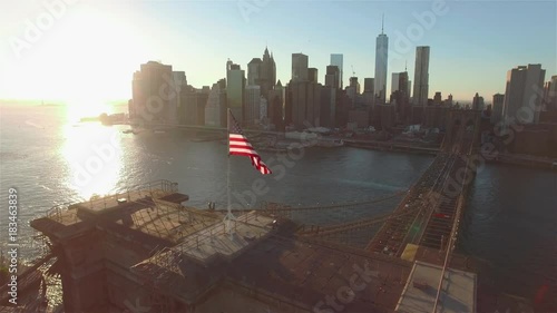 Aerial view of Brooklyn bridge at sunset. Camera almost not moving near a flapping American flag on the bridge, Manhattan panorama.